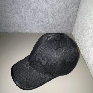 Svart keps från  med GG-mönster - Snygg svart keps   med det klassiska GG-mönstret över hela kepsen. Justerbar rem baktill i svart läder och insida i mjukt tyg. Perfekt accessoar för en stilren look.