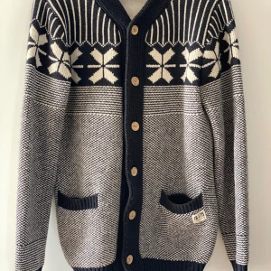 Mönstrad kofta från Jack & Jones - Säljer en snygg kofta från Jack & Jones i svart och vitt med klassiskt vintermönster och träknappar. Koftan har två fickor framtill och ribbade muddar. Perfekt för kyliga dagar.