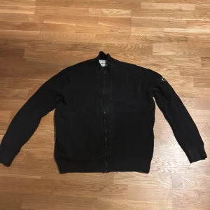 Svart zip up sweatshirt från Calvin Klein Jeans - Säljer en svart zip up från Calvin Klein Jeans i storlek M. Tröjan har dragkedja framtill och är ribbad i materialet. Enkel och stilren design med lång ärm och liten logga på ena ärmen.