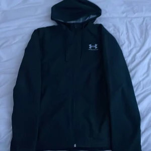 Svart Under Armour Windrbreaker - Svart Under Armour windbreaker, nypris 800kr. Använde den 1 gång och insåg att jag skulle ha köpt en mindre storlek