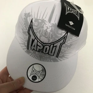  Tapout Broderi Keps  - Säljer en vit keps från Tapout med tryckt logga och grafiskt mönster framtill. Kepsen har böjd skärm och klassisk passform. Perfekt för dig som gillar sportig stil.