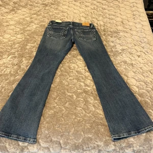 Blå bootcut jeans med broderade bakfickor - Säljer ett par klassiska blå bootcut low waist jeans med snygga broderade detaljer på bakfickorna. Jeansen är ej använda pris lapp fins kvar. 