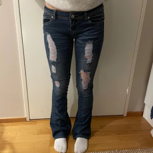 Low waist bootcut jeans  - Säljer ett par mörkblå skinny jeans med kraftiga slitningar framtill. Jeansen har klassisk femficksdesign, låg midja och detaljerade bakfickor med dekorativa sömmar. Perfekta för en avslappnad och trendig look. Midja:37 Innerbenslängd:79cm