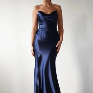 Marinblå axelbandslös långklänning i satin - Säljer en elegant marinblå långklänning i glansigt satinmaterial. Klänningen är axelbandslös med draperad överdel och figurnära passform som framhäver siluetten. Perfekt för bal eller festliga tillfällen. ( Pris kan diskuteras) I helt nytt skick, endast använd en gång! 