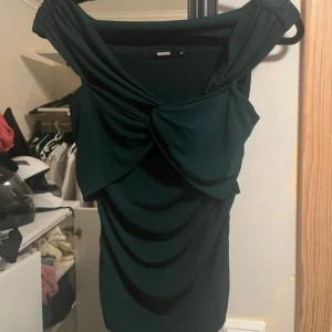 Grön topp från bikbok - Säljer en grön topp från Bik Bok med snygg drapering och stor rosettdetalj framtill. Den är även off shoulder och sitter i jättefint på!