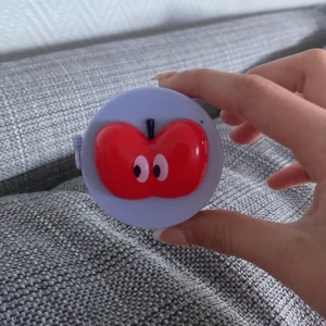 Söt måttband med äppeldesign från Cider - Ett runt måttband i ljuslila plast med en röd äppelformad dekoration med ögon på framsidan. Praktisk och gullig accessoar .Märkt med Cider och shopcider.com på baksidan.