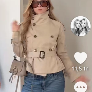 Beige trenchcoat med bälte och knappar - Stilren beige trenchcoat med hög krage, dubbelknäppning och bälte i midjan. Jackan har långa ärmar, axelklaffar och dekorativa knappar. Perfekt för en klassisk och trendig look. Bild 3 ser ni de lila defekterna 