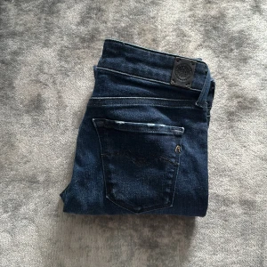 Mörkblå  jeans från Replay - Säljer ett par mörkblå jeans från Replay. Klassisk femficksmodell med dragkedja och knapp framtill. Jeansen har en mellan  passform och är tillverkade i stretchigt denimtyg för extra komfort.