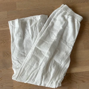 Vita vida linnebyxor - Säljer ett par luftiga och sköna vita linnebyxor med resår i midjan. Byxorna har en avslappnad passform och är perfekta för varma dagar. Materialet är lätt och har en snygg skrynklig struktur.