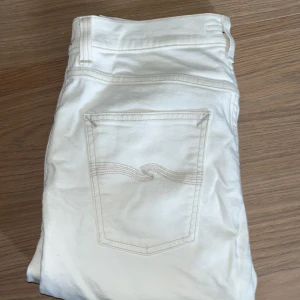 Vita jeans från Nudie Jeans 31/32 - Säljer ett par vita jeans från Nudie Jeans med klassisk femficksdesign och snygga detaljer på bakfickorna. Byxorna har normal passform och är tillverkade i bomull. Perfekta för en stilren look. Ny pris 1200 Mitt pris 650