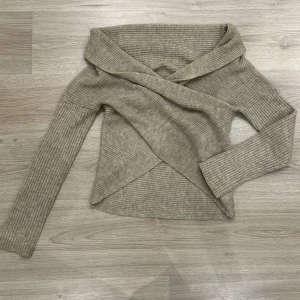 Beige omlottstickad tröja från Bubbleroom - Säljer en beige stickad tröja från Bubbleroom med omlottdesign och bred krage som funkar perfekt som off shoulder! Tröjan har lång ärm och ribbad struktur, perfekt för lager på lager. Snygg och trendig modell som passar till mycket. Den har en liten fläck på ena sidan men den går bort med en tvätt! (se sista bilden) 