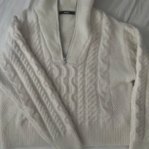 Vit stickad tröja med dragkedja från BikBok - Säljer en vit stickad tröja från BikBok i storlek M. Tröjan har kabelstickat mönster, hög krage och dragkedja.