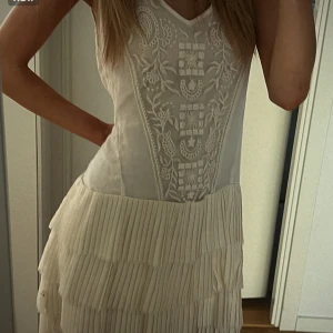 Vit klänning med spets och plisserad kjol - Säljer en superfin vit klänning med v-ringning, spetsdetaljer upptill och plisserad kjol. Klänningen har ärmlös design och romantiska broderier framtill. Perfekt för sommarens alla tillfällen!💋💋💋