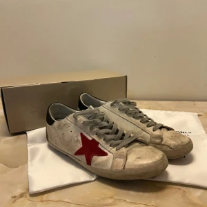 Golden goose skor - Snygga vita Golden goose skor med röd stjärna på sidan. Skorna har grå snörning och en svart häl. De är ganska använda och därav priset. Vid fler frågor eller bilder, kontakta.