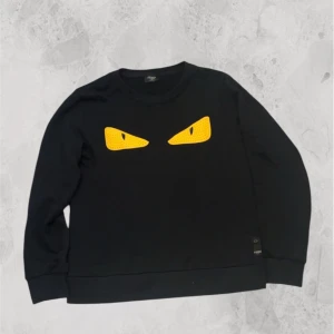 Fendi monster eyes - Cool svart sweatshirt från Fendi med ikoniska gula ögon framtill. Tröjan har rund halsringning och ribbade muddar vid ärmslut och nederkant. Tillverkad i Italien och känns riktigt lyxig och unik. Inga defekter, riktigt fint skick!