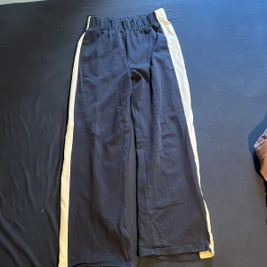 Mörk blåa vida mjukisbyxor med vita revärer - Svarta mjukisbyxor med breda ben och vita revärer längs sidorna. Resår i midjan för extra komfort. Perfekta för en avslappnad stil eller till träning.