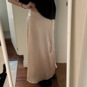 Beige satinkjol - Säljer en lång, beige/guldig satinkjol med snygg glansig finish. Kjolen har en rak och elegant passform som faller fint längs kroppen. Perfekt för dig som gillar en stilren och trendig look.