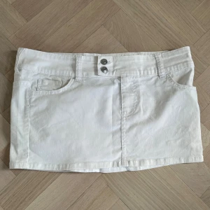 Vit jeanskjol med fickor - Säljer en vit kort jeanskjol med klassiska fickor fram och bak samt dubbla knappar i midjan. Kjolen har en rak passform och är perfekt för en fräsch och stilren look. Säljer för att den är för stor💕