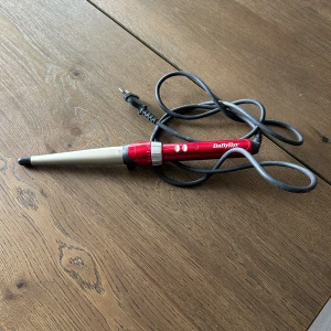 Locktång från BaByliss - En konformad locktång från BaByliss i rött och silver med svart spets. Perfekt för att skapa naturliga lockar och vågor. Utrustad med sladd och justerbar temperatur. Smidig design som gör den enkel att använda. Använd ytterst lite