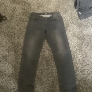 Grå jeans från Jack & Jones - Snygga grå jeans från Jack & Jones med klassisk femficksdesign och raka ben. Byxorna har knappgylf och diskret logga på bakfickan. Perfekta för en stilren vardagslook.