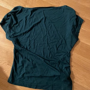 Mörkgrön topp från SHEIN - Det En enkel mörkgrön topp från SHEIN med korta ärmar och rund halsringning. Tillverkad i ett mjukt och stretchigt material som sitter bekvämt mot kroppen. Perfekt att matcha med jeans eller kjol.