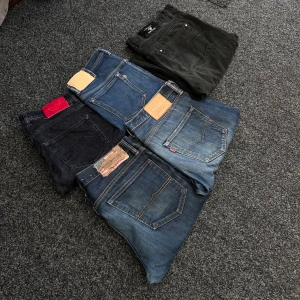En bunt av märkes jeans  - Säljer fem par jeansbyxor i olika blå och svarta nyanser. Några har klassiska Levis-lappar och synliga sömmar. Modellerna varierar mellan raka och något smalare ben. Perfekta för dig som gillar klassiska jeans med olika passform och detaljer.