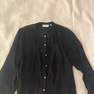 Svart skjorta med spets från Viveca N - Svart skjorta från Viveca N i storlek 40. Skjortan har långa ärmar, knappar framtill och snygga spetsdetaljer vid bröstet. Enkel och stilren design som passar perfekt till jeans eller kjol.