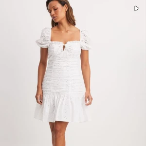 Vit kort klänning från NA-KD - Superfin vit kort klänning från NA-KD med broderade blommor, puffärmar och volang nertill. Klänningen har söt knytning framtill och är gjord i bomull med romantisk känsla. Perfekt för sommarens alla tillfällen! nypris 600kr💕