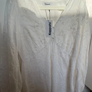 Vit klänning - student klänning   - Säljer en vit klänning från Kappahl med v-ringning och fina broderade blommönster. Klänningen har långa ärmar och tre dekorativa knappar framtill. Perfekt för studenten/ sommaren/ skolavslutningen 