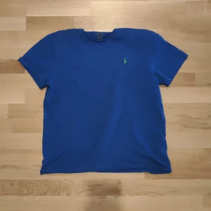 Blå t-shirt från Polo Ralph Lauren - Säljer en klassisk blå t-shirt från Polo Ralph Lauren med rund halsringning och liten grön broderad logga på bröstet.