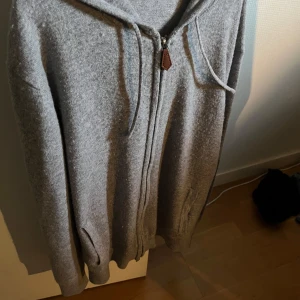 Grå cashmere zip hoodie från Sayless - Mysig grå hoodie från Sayless i mjuk cashmere. Tröjan har dragkedja framtill, huva med dragsko och ribbade muddar. Perfekt för en avslappnad och stilren look. 