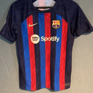 FC Barcelona Lewandowski tröja XL Nike - Säljer en officiell FC Barcelona matchtröja från Nike med Lewandowski och nummer 9 på ryggen. Tröjan är kortärmad, har klassiska blå och röda ränder, klubbmärke, Nike-logga och Spotify som sponsor. Tillverkad i Dri-FIT-material som andas.