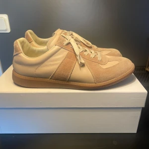 Maison margiela sneakers - Snygga beige sneakers med paneler i mocka och slätt skinn, klassisk design och gummisula. Skorna har rund tå, snörning och neutrala toner som passar till det mesta. Perfekta för dig som gillar stilrena och minimalistiska sneakers.
