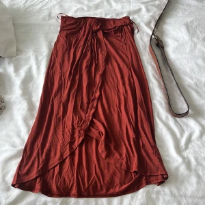 Rostbrun omlottkjol från Pieces - Säljer en rostbrun långkjol från Pieces i mjuk bomull. Kjolen har omlottmodell med knyt i midjan och snyggt fall. Perfekt för dig som gillar en chill och trendig stil. Passar till sneakers eller sandaler.