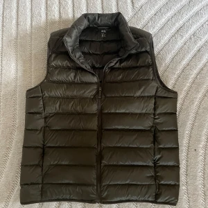 Grön dunväst från Uniqlo Ultra Light Down - Säljer en grön, lätt och quiltad dunväst från Uniqlo Ultra Light Down. Västen har hög krage, dragkedja framtill och horisontella sömmar. Perfekt för lager-på-lager och enkel att bära med sig tack vare den smidiga designen.