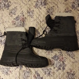 Svarta vinterkängor med foder - Rejäla svarta vinterkängor med tjock sula och vitt foder upptill. Kängorna har snörning framtill och är perfekta för kalla dagar. Grov sula ger bra grepp och värmande insida håller fötterna varma. Oanvända