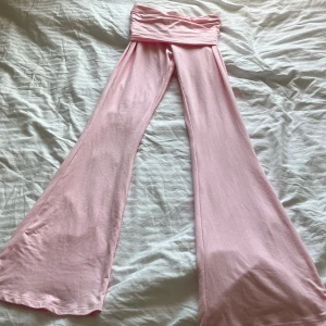 Ljusrosa utsvängda byxor med hög midja - Säljer ett par ljusrosa byxor med extra hög midja och utsvängda ben. Byxorna är tillverkade i mjukt stretchigt material och passar perfekt för en avslappnad och trendig stil.