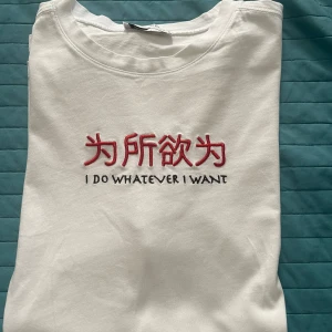 Vit t-shirt med broderad text - Vit t-shirt med röd broderad japansk text och svart texten 'I DO WHATEVER I WANT' på bröstet. Klassisk rund hals och korta ärmar. T-shirten är i mjuk bomull och har en clean, minimalistisk vibe med en cool statement-detalj framtill.Som man ser på bild nr 4 och 5 finns en mörk fläck som kan inte tas bort därav det låga priset.