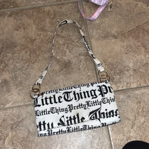 PrettyLittleThing axelväska med tryck - Cool axelväska från PrettyLittleThing i vitt med svart textprint över hela väskan. Väskan har guldfärgade metalldetaljer och magnetlås. Perfekt storlek för mobilen och det viktigaste. Snygg och trendig accessoar till din outfit.