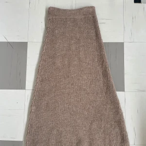 Beige stickad långkjol från Gina Tricot - Mysig beige stickad långkjol från Gina Tricot i ribbat material. Kjolen har en rak och något utsvängd passform som ger en chill vibe. Perfekt att styla med chunky boots eller sneakers för en trendig look. 