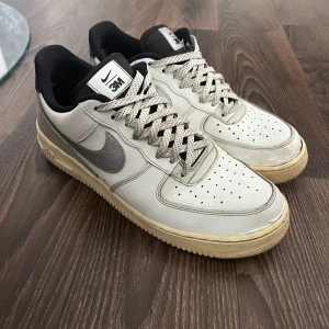 Nike Air Force 1 3M vit/silver sneakers - Nike Air Force 1 sneakers i samarbete med 3M. Skorna är vita med silverdetaljer, reflekterande paneler och svart häl. Perforerad tå, gräddvit sula och klassisk snörning. Swoosh-logga i silver och 3M-märke på plösen. Perfekta för dig som gillar unika detaljer.