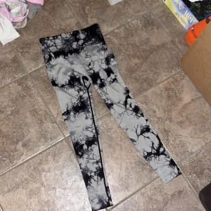 Svarta och grå tie-dye leggings S - Snygga leggings i svart och grått tie-dye mönster. Hög midja och scrunch-detalj bak för extra shaping. Tillverkade i stretchigt material med 90% polyamid och 10% elastan, perfekta för träning eller chill.