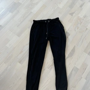 Svarta mjukisbyxor från Freequent - Svarta mjukisbyxor från Freequent med resår i midjan och dragsko. Byxorna har raka ben och är tillverkade i ett mjukt, sammetsliknande material. Perfekta för en avslappnad stil.