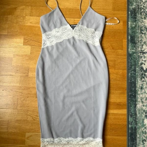 Spetsklänning från Missguided - Jättesnygg ljusgrå klänning från Missguided med spetsdetaljer, v-ringning och smala axelband. Aldrig använd – min mammas fina klänning som förtjänar att bäras!