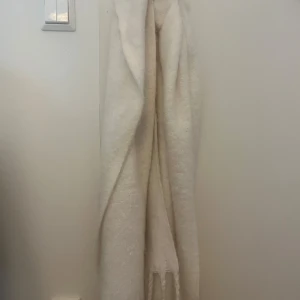 Vit fluffig halsduk med text - Supermjuk och fluffig vit halsduk med ljusrosa texten 'ICONIC 1971' längs ena kanten. Halsduken har fransar i ändarna och är perfekt att vira flera varv runt halsen för extra mysfaktor. Enkel och stilren design som lyfter vilken outfit som helst. Ny pris 199kr