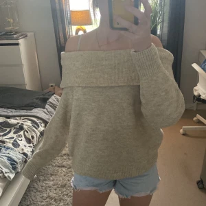 Beige offshoulder stickad tröja - Supermysig beige stickad tröja med bred offshoulder-krage. Tröjan har en loose passform och långa ärmar, perfekt för dig som gillar en chill och avslappnad stil. Passar grymt till både jeans och kjol för en trendig look.