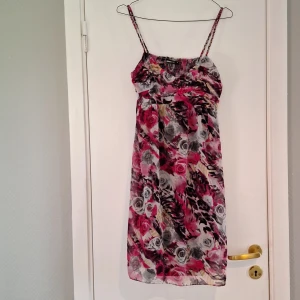 Blommig kortklänning från Gina Tricot - Supersöt kortklänning med smala axelband från Gina Tricot. Klänningen har ett färgstarkt blommigt mönster. Lätt och luftig modell med smock i ryggen och v-ringad hals. Perfekt för varma dagar!
