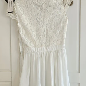 Ny Vit spetsklänning från NLY One - Superfin vit klänning från NLY One med spets upptill och lätt, flowig kjol. Klänningen har ärmlös design och v-ringning, perfekt för sommarens tillfällen. Spetsdetaljerna ger en romantisk känsla och kjolen faller snyggt. Studentklänning 