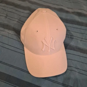Vit keps från New Era med NY-logga - Säljer en stilren vit keps från New Era med broderad NY-logga framtill. Kepsen är i bomull och har klassisk böjd skärm. Perfekt accessoar för en sportig look.