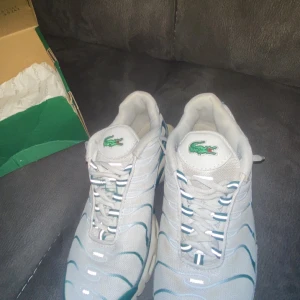 Nike Air Max Plus Tn X Lacoste collab sneakers i vitt och turkos - Nike Air Max Plus Tn X Lacoste sneakers i vitt och turkos med klassisk Tn Air-detalj på hälen. Skorna har snörning, rund tå och synlig Air Max-dämpning i sulan. Swoosh-logga på sidan och meshmaterial för extra andningsförmåga.